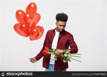 Handsome African American holding heart balloon and checking time on his watch. Handsome African American holding heart balloon and checking time on his watch.