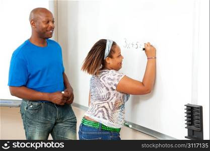 Handsome african-american math teacher works with a student at the board.