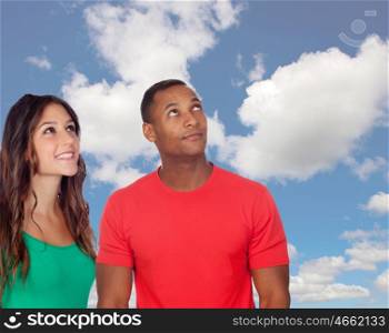 Handsome african guy and his caucasian girl looking up with a blue sky of background