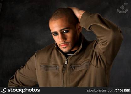 Handsome African Hispanic guy frowning with strong macho expression and dark eyes in green vest and hand on head