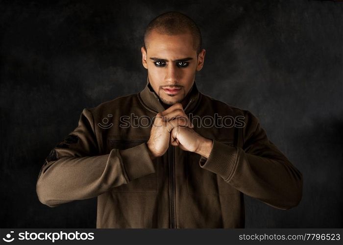 Handsome African Hispanic guy frowning with strong mad macho expression and dark eyes in green vest and hands in a fist