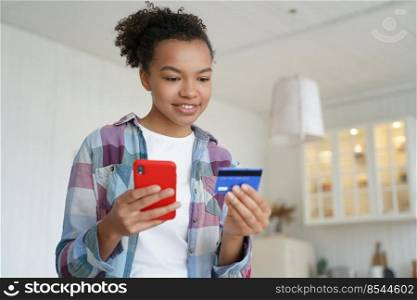 Handsome afro girl is buying online with smartphone and credit card. Happy teenager spends money through internet banking. Online shopping with credit card. Ecommerce and consumerism concept.. Happy teenager spends money from credit card. Online shopping, ecommerce and consumerism.