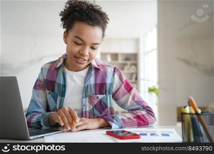 Handsome afro schoolgirl is studying remote at home and doing homework. Teenage girl is sitting at the desk in front of computer having online exam. Remote study at school or college via zoom.. Handsome afro schoolgirl is studying remote at home and doing homework. Online exam.
