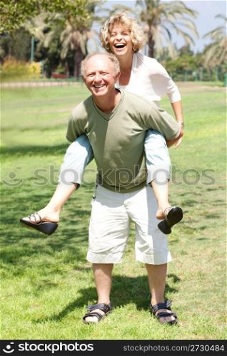 Handsome aged man gives his lovable wife piggy-ride