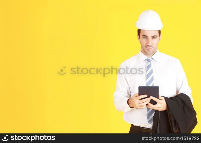 Handsome and smart engineer in suit and white shirt and Wearing a white safety engineer hat with hand holding smartphone isolated on yellow background. Copy Space