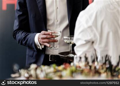 Handsome and successful businessman in stylish suit holding glass of martini on party, corporate party, conference, forums, banquets, closeup. selective focus.. Handsome and successful businessman in stylish suit holding glass of martini on party, corporate party, conference, forums, banquets, closeup. selective focus