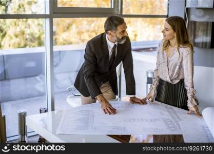 Handsome architect and his young female colleague checking plans and blueprints in the office