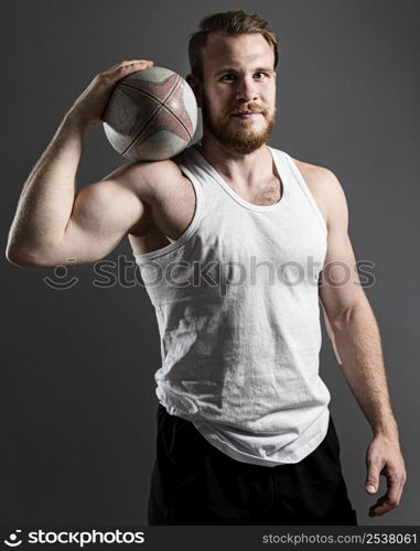 handsome athletic male rugby player holding ball while posing