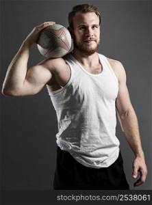 handsome athletic male rugby player holding ball while posing