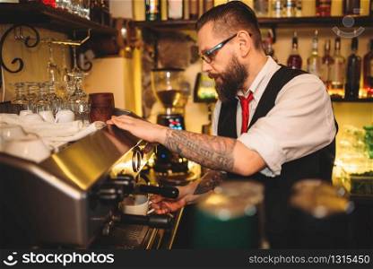 Handsome barista preparing cup of coffee in espresso machine behind bar counter
