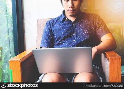 Handsome bearded Asian man working at cafe while sitting on the sofa.Concept of young people using laptop computer. Flare light background