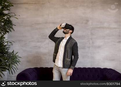 Handsome bearded young man wearing virtual reality goggles in modern room