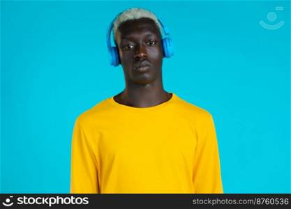 Handsome black man with trendy hairdo and headphones in studio against blue background. Guy in yellow outfit. Music, dance, radio concept. Handsome black man with trendy hairdo and headphones in studio against blue background. Guy in yellow outfit. Music, dance, radio concept.