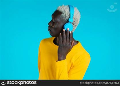 Handsome black man with trendy hairdo and headphones in studio against blue background. Guy in yellow outfit. Music, dance, radio concept. Handsome black man with trendy hairdo and headphones in studio against blue background. Guy in yellow outfit. Music, dance, radio concept.