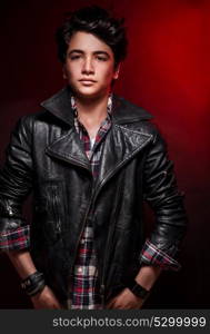 Handsome boy portrait over red background, wearing leather jacket and stylish shirt, fashionable autumn clothes, funky teens fashion