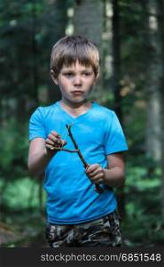 Handsome boy with makeshift slingshot in summer forest