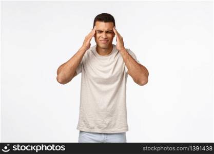 Handsome brazilian guy suffering terrible headache, grimacing from pain, squinting and touching temples, have migraine or ache from hangover, standing white background, feeling not well.. Handsome brazilian guy suffering terrible headache, grimacing from pain, squinting and touching temples, have migraine or ache from hangover, standing white background, feeling not well