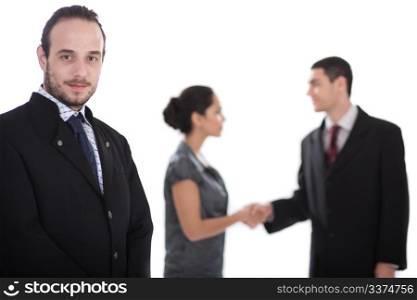 Handsome business man looking at us, two collegues giving shakehand out of focus in isolated white background