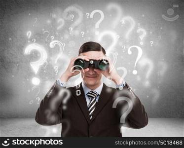 Handsome business man with binoculars and question marks above his head