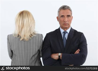 handsome businessman cross-armed and female businesspartner with back turned to camera