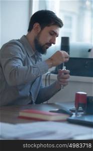 Handsome businessman filling electronic cigarette with liquid in office