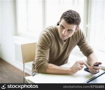 Handsome businessman holding cell phone while looking away in office