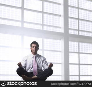 Handsome businessman is relaxing in the office, sitting in a traditional yoga lotus position.