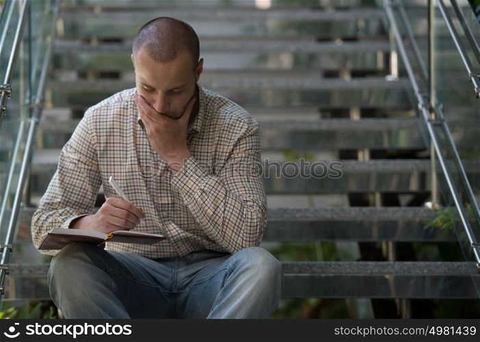 Handsome businessman making notes sitting on stairs inside office building