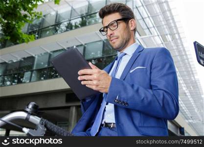 handsome businessman on bicycle wearing glasses and using tablet