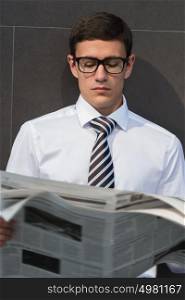 Handsome businessman or manager, in front of modern office architecture, reading newspaper