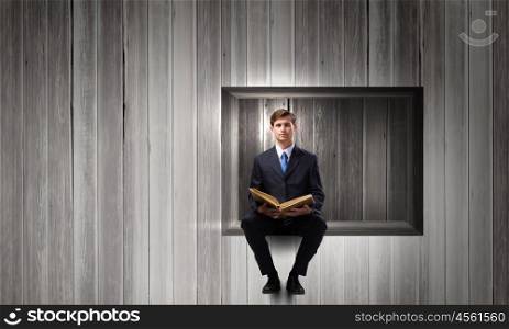 Handsome businessman sitting in cube and reading book