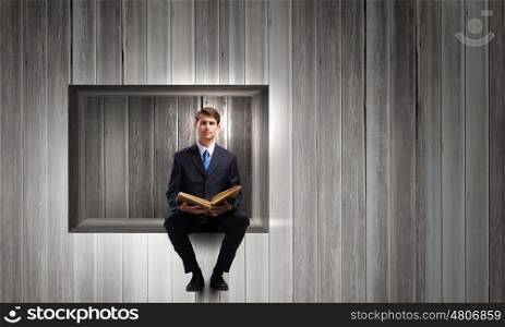 Handsome businessman sitting in cube and reading book