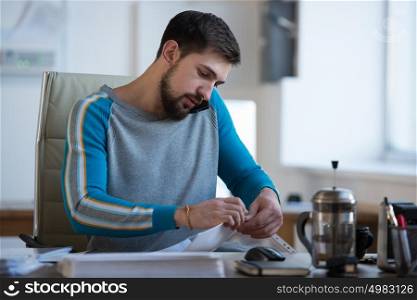 Handsome businessman working in office on the phone and doing paperwork he is very busy