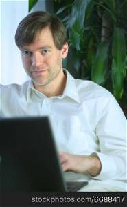 Handsome businessman working on laptop in casual attire.