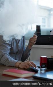 Handsome businessman working with computer in office and vaping electronic cigarette