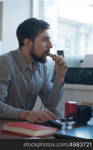 Handsome businessman working with computer in office and vaping electronic cigarette