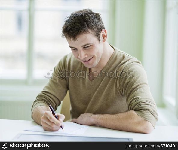 Handsome businessman writing on document at desk in office