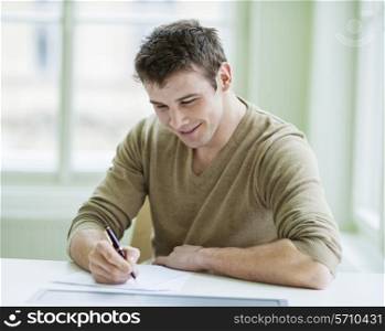 Handsome businessman writing on document at desk in office
