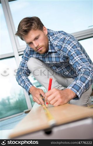 handsome carpenter measuring wood using a tape measure and pencil