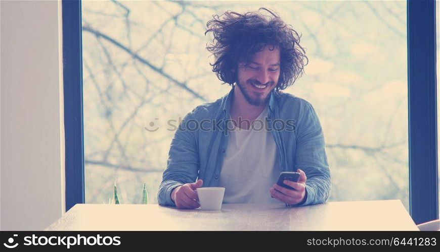 Handsome casual young man drinking coffee and using a mobile phone at home