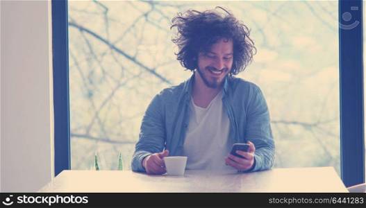 Handsome casual young man drinking coffee and using a mobile phone at home