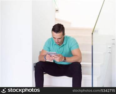 Handsome casual young man using a tablet while sitting on the stairs at home