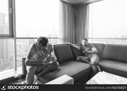 Handsome casual young men using a mobile phones near the window at home. two young men using a mobile phones at home