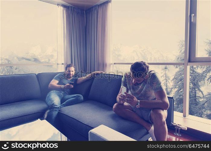 Handsome casual young men using a mobile phones near the window at home. two young men using a mobile phones at home
