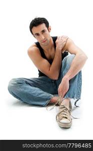 Handsome Caucasian guy wearing black tank top and jeans sitting on floor holding shoulder, isolated