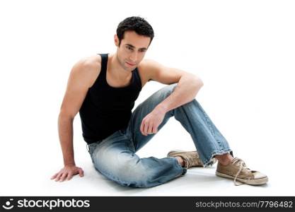 Handsome Caucasian guy wearing black tank top and jeans sitting on floor looking down, isolated