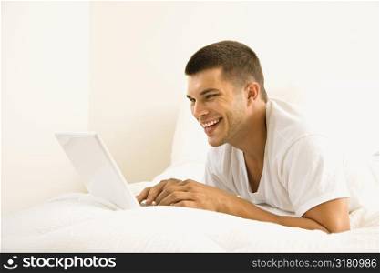 Handsome Caucasian mid adult man lying in bed with laptop.