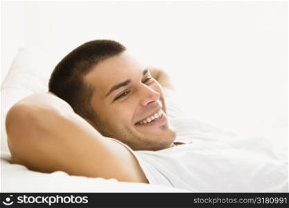 Handsome Caucasian mid adult man lying with hands behind head and smiling.