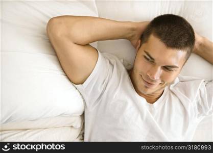 Handsome Caucasian mid adult man lying with hands behind head smiling.