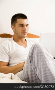 Handsome Caucasian mid adult man sitting in bed with laptop.